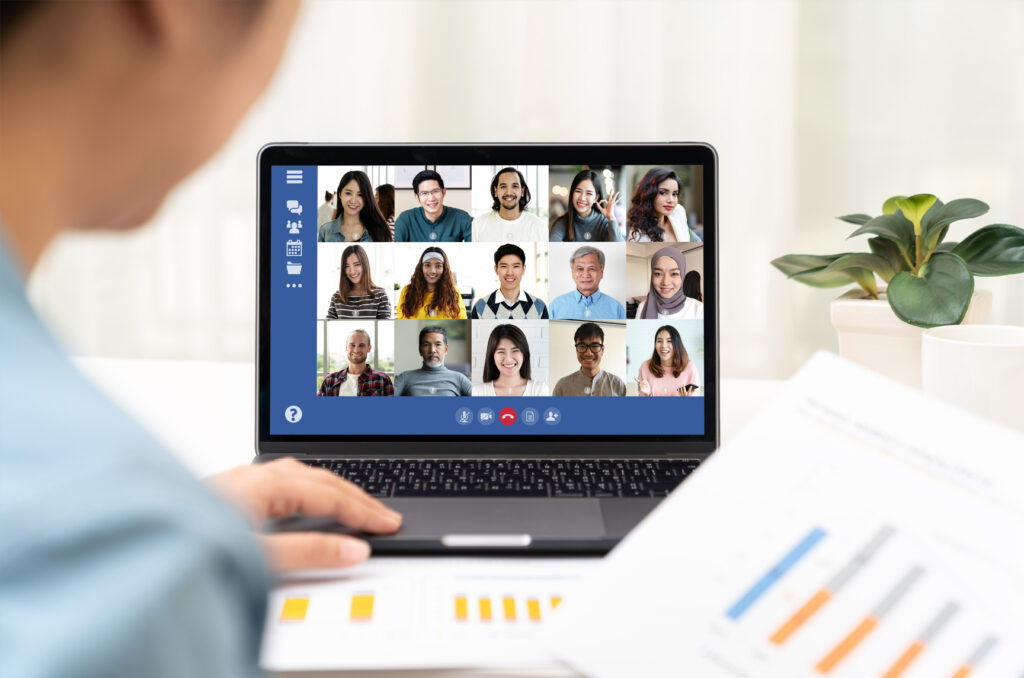 Young Asian businesswoman participating in a video conference from home with her team displayed on laptop screen.