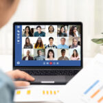 Young Asian businesswoman participating in a video conference from home with her team displayed on laptop screen.