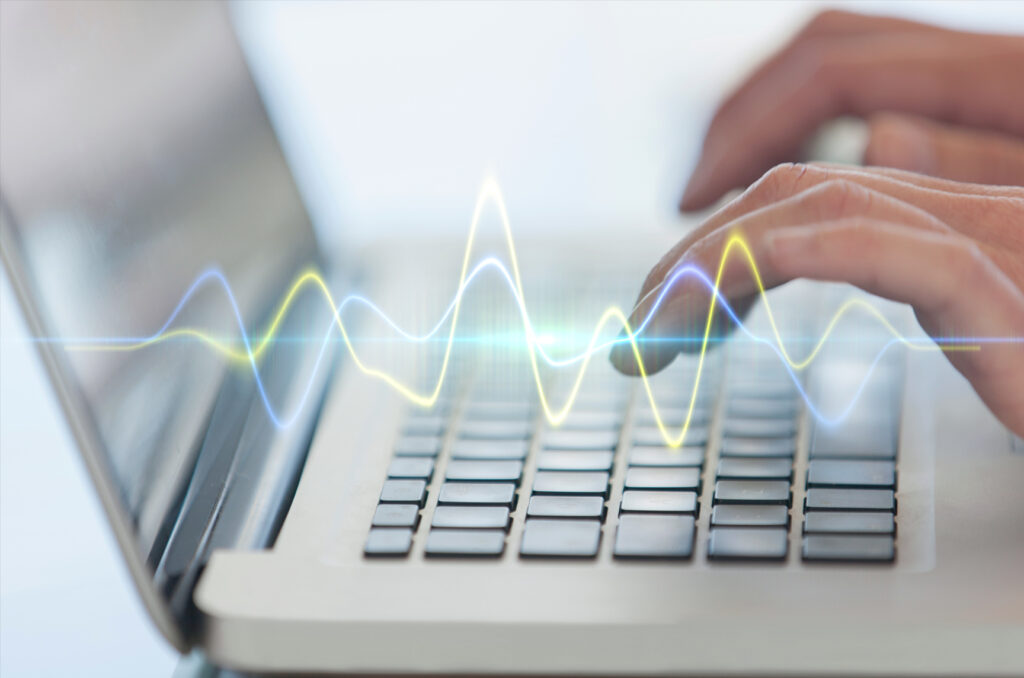 Hands typing on a laptop with a soundwave, symbolizing digital accessibility.