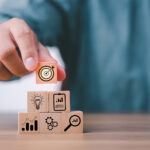 Hand stacking wood blocks with business strategy icons for annual report concept.