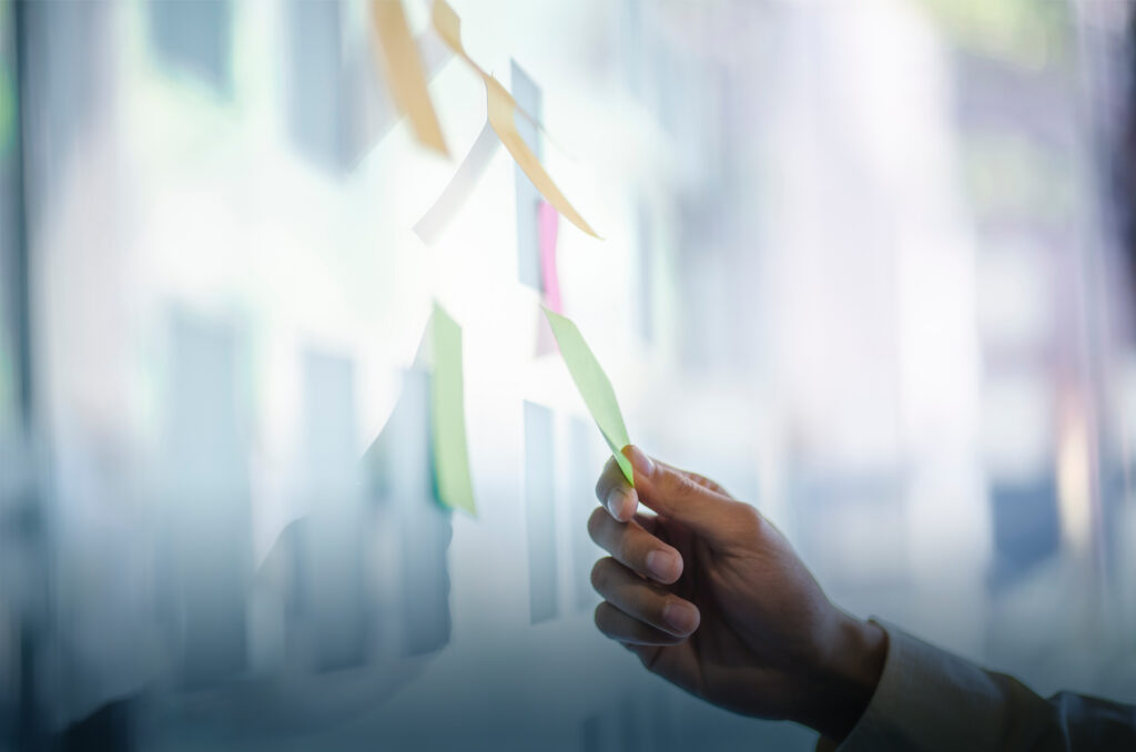 Businessman placing a sticky note on glass wall as a reminder for project management concept.