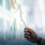 Businessman placing a sticky note on glass wall as a reminder for project management concept.